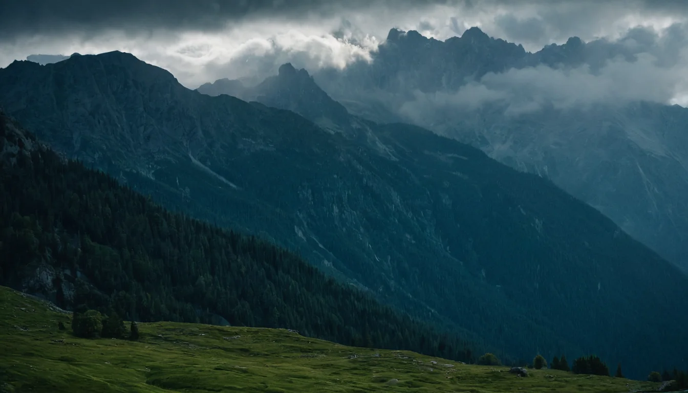 A dark mountain range with clouds and a green meadow in the foreground