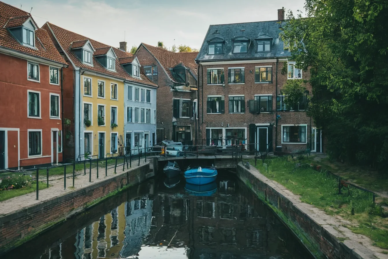 Colorful historic houses line a calm canal with a blue boat and tree-lined banks.
