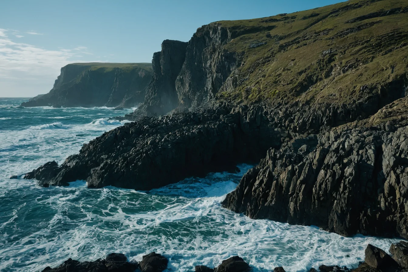 Rugged cliffs meet crashing ocean waves under a clear blue sky