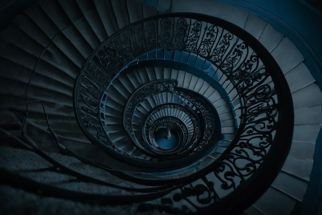 Spiral staircase with ornate iron railings and blue-tinted stone steps in dim light