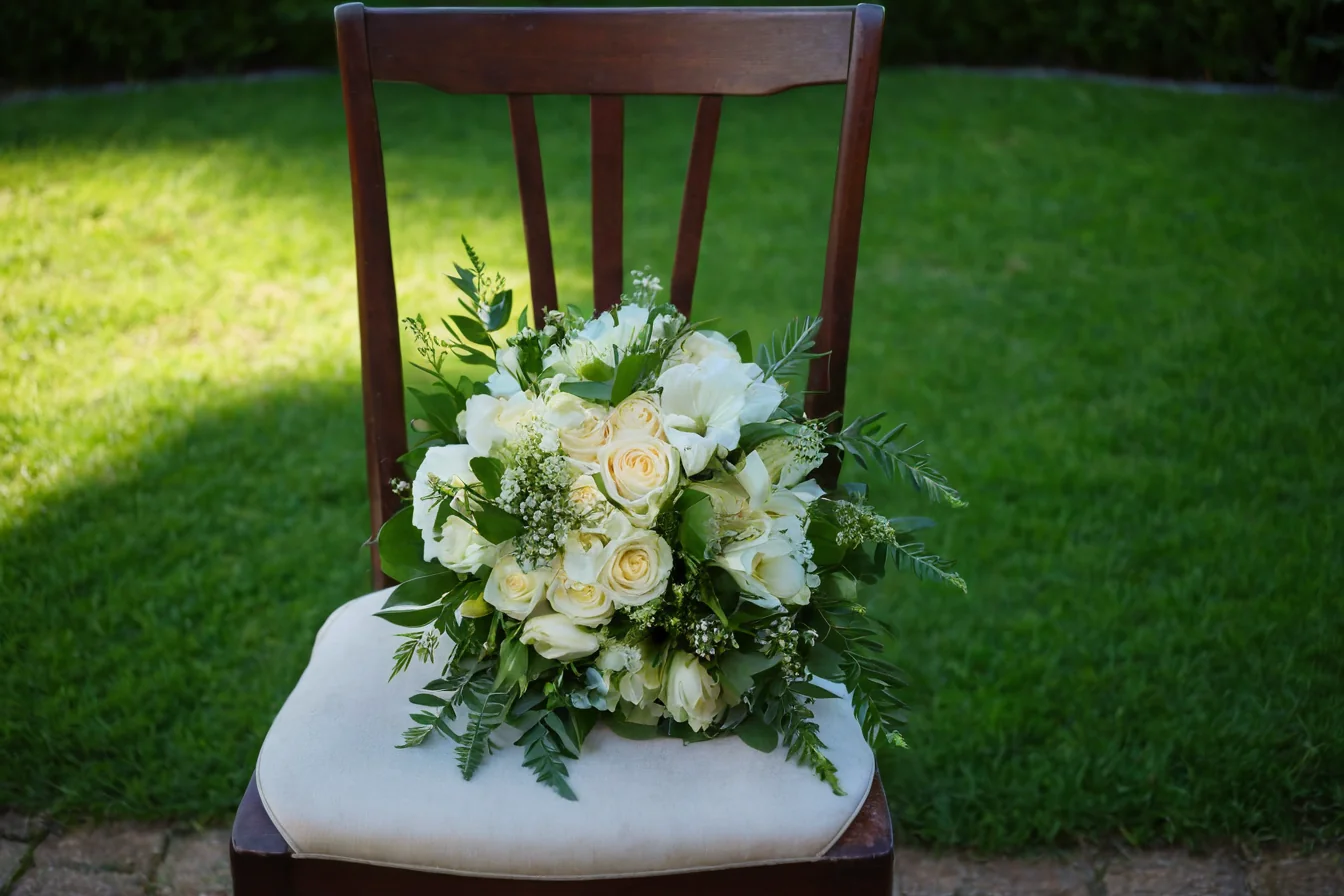 White rose bouquet with greenery on a wooden chair with cream cushion outdoors on grass